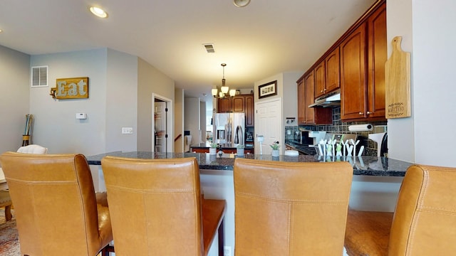 kitchen with a chandelier, dark countertops, under cabinet range hood, visible vents, and stainless steel appliances