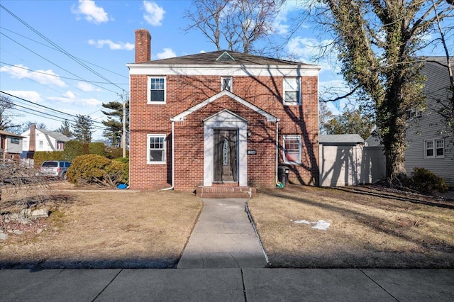 view of front facade with brick siding, a chimney, and a front lawn