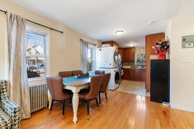 dining space featuring baseboards, light wood finished floors, stacked washing maching and dryer, and radiator