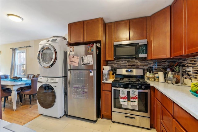 kitchen featuring stainless steel appliances, light countertops, backsplash, brown cabinets, and stacked washer and clothes dryer