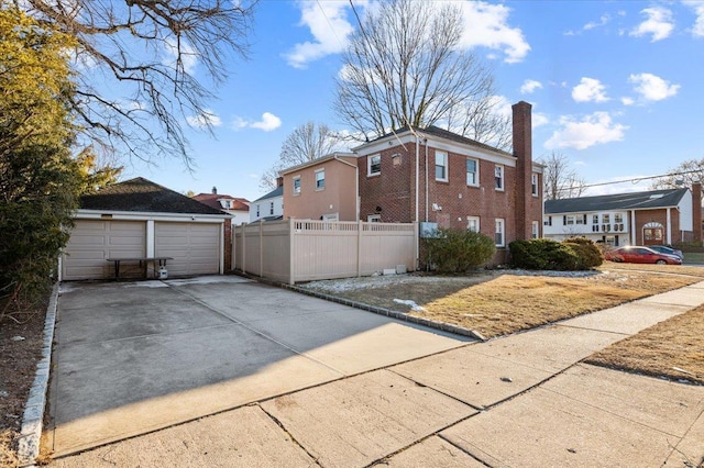 view of side of property featuring a chimney, a detached garage, fence, an outdoor structure, and brick siding