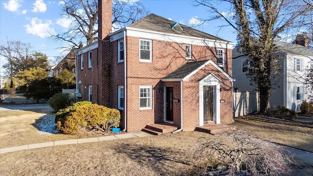 view of front of house with brick siding, a chimney, and fence