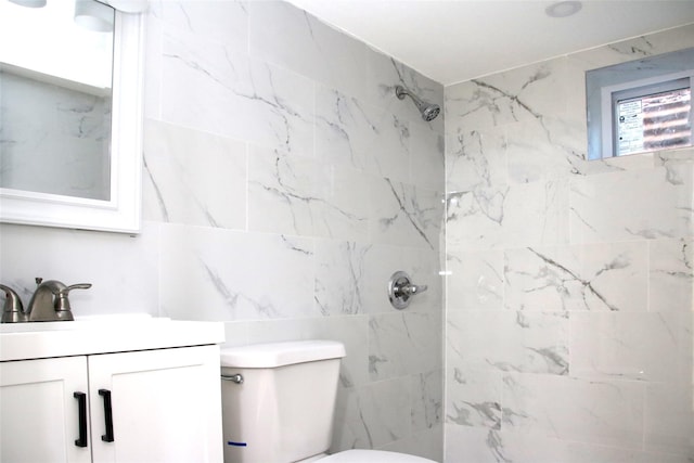 bathroom with tiled shower, vanity, toilet, and tile walls