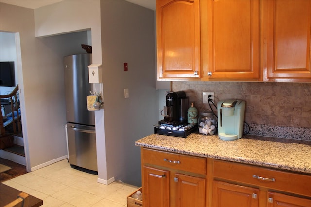 kitchen with light stone countertops, light tile patterned floors, stainless steel refrigerator, and decorative backsplash