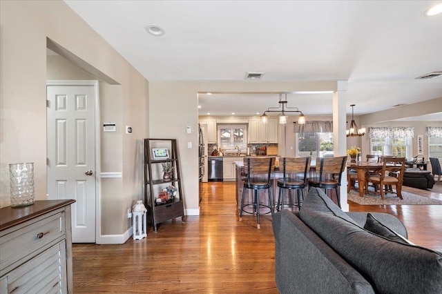 living room featuring ornate columns, sink, hardwood / wood-style floors, and an inviting chandelier