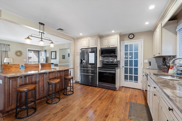 kitchen with sink, a kitchen bar, hanging light fixtures, light stone counters, and stainless steel appliances