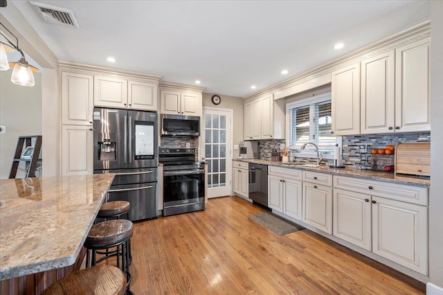 kitchen featuring sink, hanging light fixtures, stainless steel appliances, light hardwood / wood-style floors, and a kitchen bar