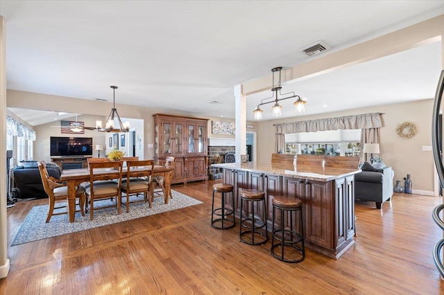 kitchen featuring a kitchen bar, hanging light fixtures, light wood-type flooring, a center island with sink, and light stone countertops