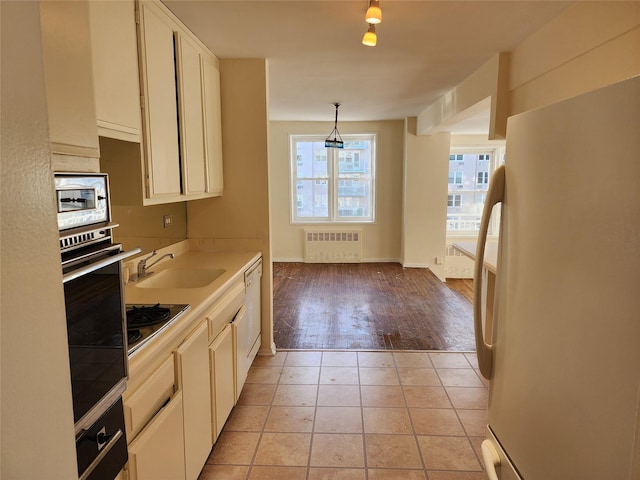 kitchen featuring sink, white cabinetry, hanging light fixtures, radiator heating unit, and stainless steel appliances