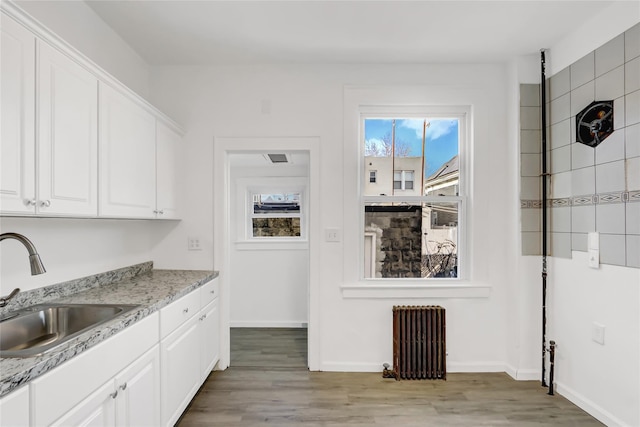 kitchen featuring white cabinetry, radiator heating unit, light hardwood / wood-style floors, and sink