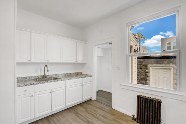 kitchen with sink, white cabinetry, light stone counters, light hardwood / wood-style flooring, and radiator