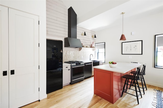 kitchen with a kitchen island, a kitchen bar, wall chimney exhaust hood, black appliances, and light hardwood / wood-style flooring