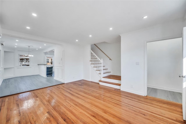 unfurnished living room featuring crown molding, an inviting chandelier, and light hardwood / wood-style flooring