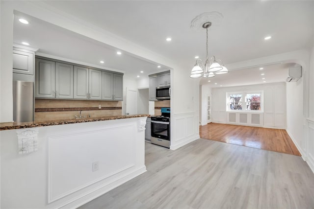 kitchen with light hardwood / wood-style flooring, gray cabinets, appliances with stainless steel finishes, a wall mounted AC, and a chandelier