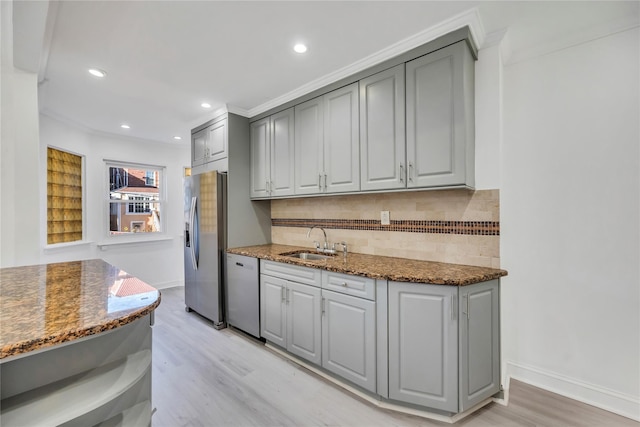 kitchen with sink, light hardwood / wood-style flooring, appliances with stainless steel finishes, gray cabinetry, and dark stone countertops