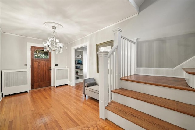 entrance foyer with ornamental molding, radiator heating unit, light hardwood / wood-style floors, and a chandelier