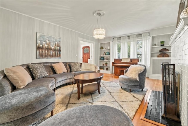 living room with a fireplace, built in features, light hardwood / wood-style floors, and a chandelier