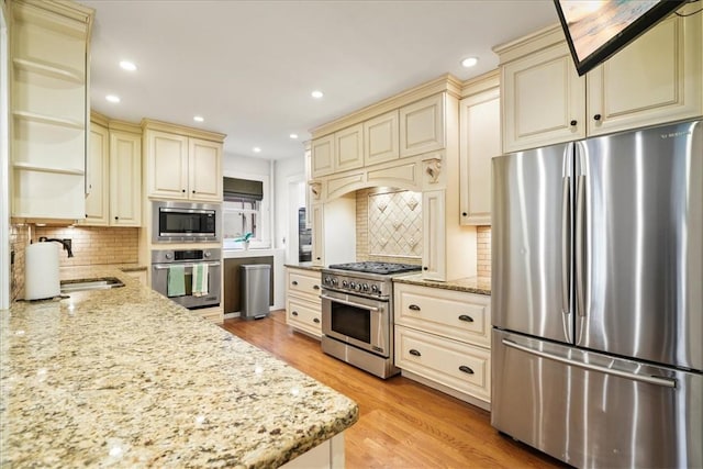 kitchen with appliances with stainless steel finishes, light stone counters, cream cabinets, and light hardwood / wood-style floors