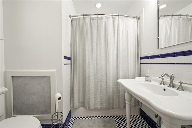 bathroom with toilet, curtained shower, sink, and tile walls