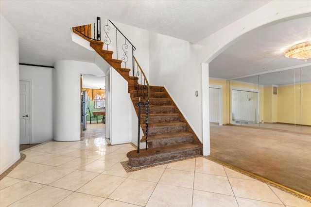 stairway with tile patterned flooring, crown molding, and a textured ceiling