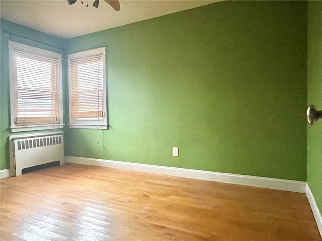 empty room featuring radiator heating unit, light hardwood / wood-style floors, and ceiling fan