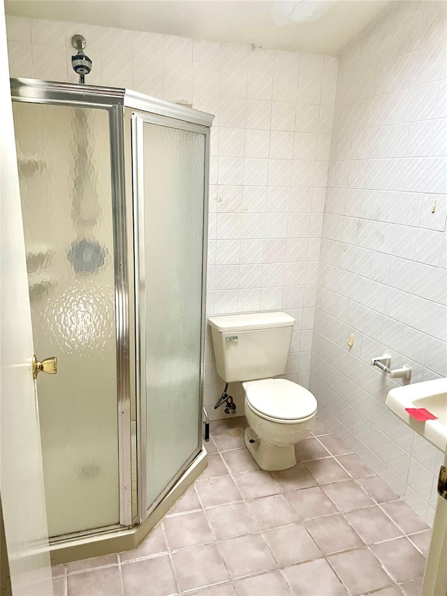 bathroom featuring tile patterned floors, toilet, a shower with door, and tile walls