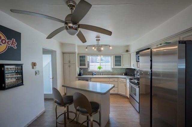 kitchen with appliances with stainless steel finishes, a kitchen island, tasteful backsplash, a kitchen bar, and light wood-type flooring