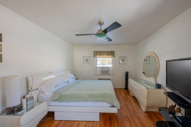 bedroom featuring cooling unit, ceiling fan, radiator heating unit, and light hardwood / wood-style flooring