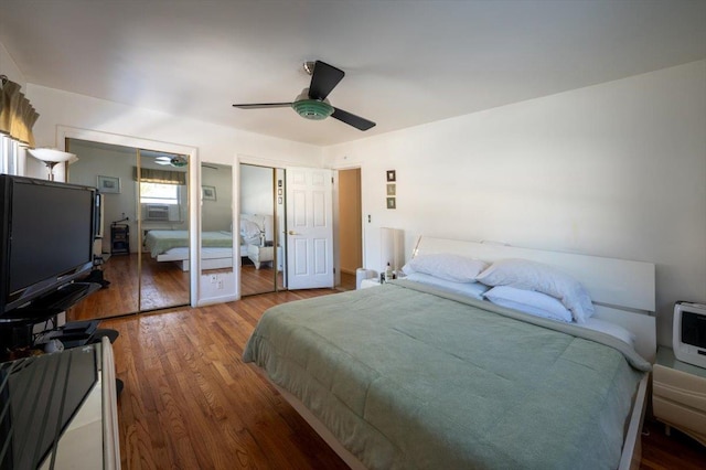 bedroom featuring cooling unit, ceiling fan, wood-type flooring, and multiple closets