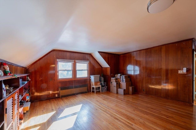 additional living space with lofted ceiling, radiator heating unit, wood walls, and light hardwood / wood-style flooring