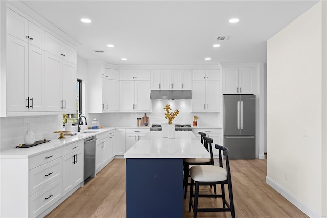 kitchen with a kitchen island, appliances with stainless steel finishes, white cabinetry, sink, and a kitchen bar