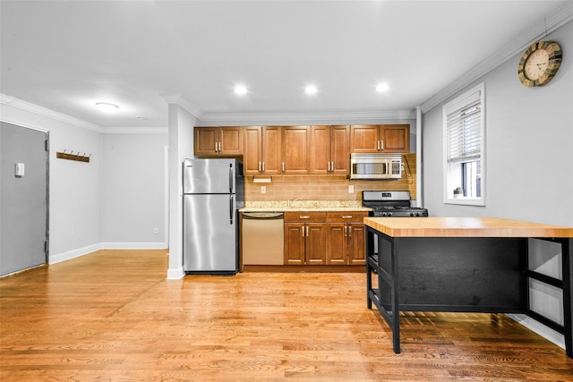 kitchen with crown molding, decorative backsplash, light wood-type flooring, and appliances with stainless steel finishes