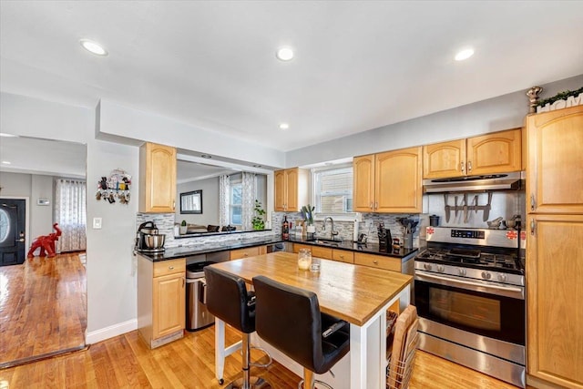 kitchen featuring sink, light wood-type flooring, decorative backsplash, stainless steel range with gas cooktop, and light brown cabinets