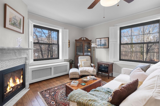 living room featuring a tile fireplace, radiator, ornamental molding, ceiling fan, and dark wood-type flooring