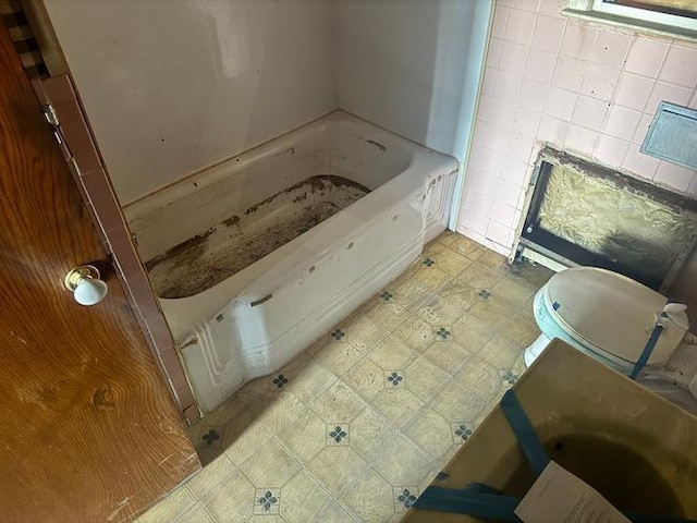 bathroom featuring tile patterned floors, toilet, tile walls, and a washtub