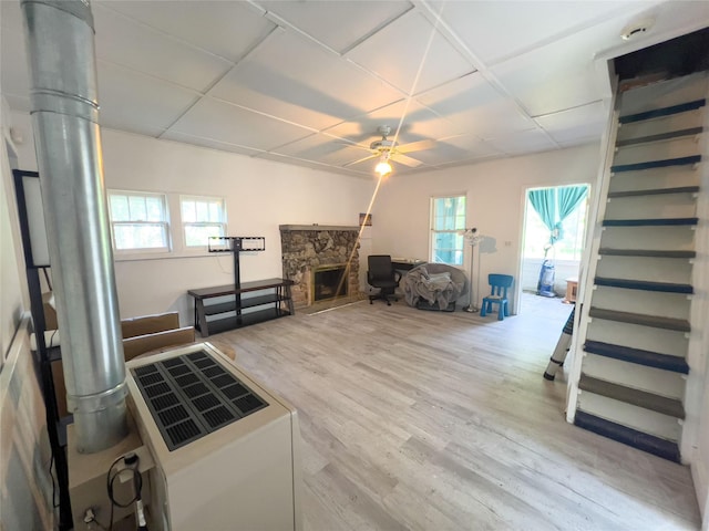 living room with ceiling fan, plenty of natural light, a stone fireplace, and light hardwood / wood-style flooring