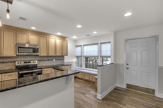 kitchen with dark stone counters, pendant lighting, stainless steel appliances, hardwood / wood-style floors, and backsplash