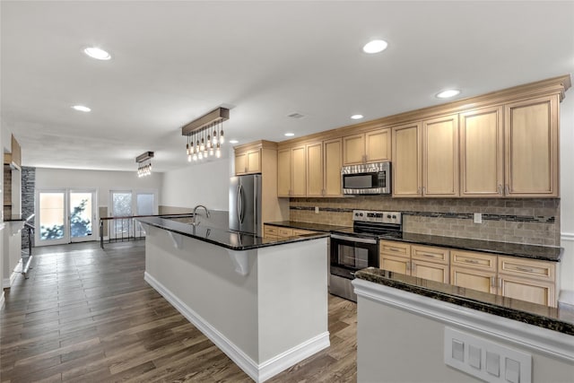 kitchen featuring dark wood-type flooring, tasteful backsplash, dark stone countertops, appliances with stainless steel finishes, and pendant lighting