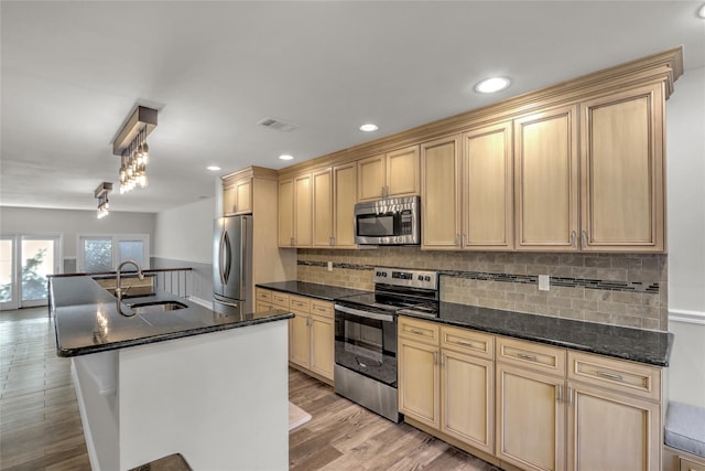 kitchen featuring sink, tasteful backsplash, light hardwood / wood-style floors, stainless steel appliances, and a kitchen island with sink