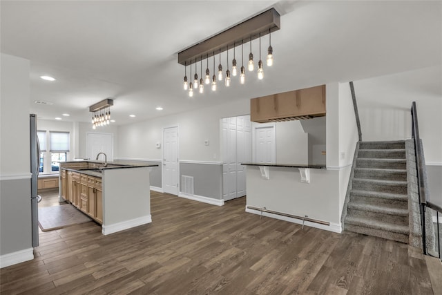 kitchen with a kitchen bar, sink, hanging light fixtures, dark hardwood / wood-style flooring, and a kitchen island with sink