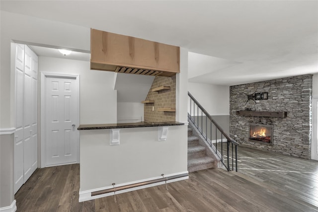 kitchen featuring dark stone countertops, dark wood-type flooring, a fireplace, and kitchen peninsula