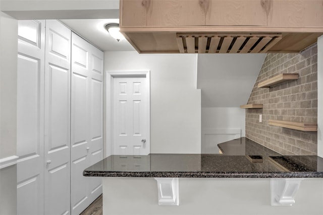 kitchen with dark stone countertops, decorative backsplash, and kitchen peninsula