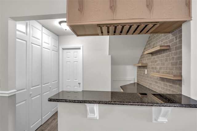 kitchen featuring tasteful backsplash, dark wood-type flooring, dark stone countertops, and kitchen peninsula