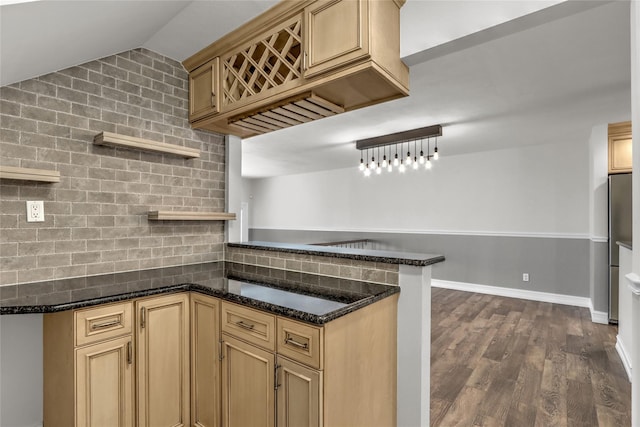 kitchen with stainless steel refrigerator, lofted ceiling, dark stone countertops, kitchen peninsula, and dark wood-type flooring