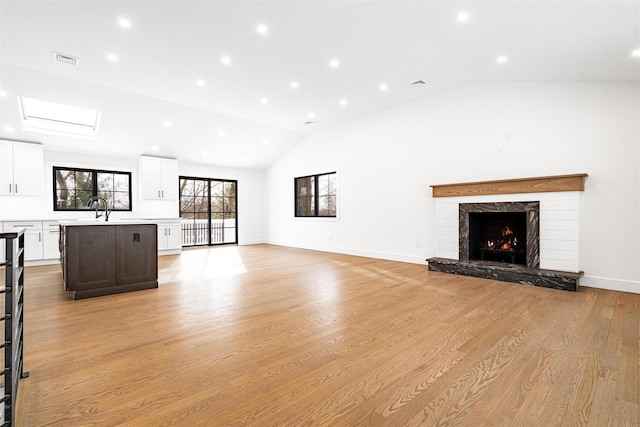 unfurnished living room with sink, a high end fireplace, light hardwood / wood-style floors, and vaulted ceiling