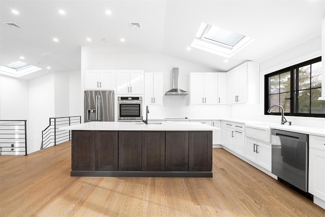 kitchen with wall chimney exhaust hood, appliances with stainless steel finishes, a center island with sink, and white cabinets