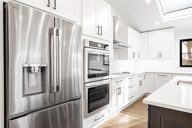 kitchen featuring wall chimney range hood, light hardwood / wood-style floors, white cabinets, and appliances with stainless steel finishes