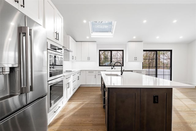 kitchen with light hardwood / wood-style flooring, white cabinetry, black electric stovetop, an island with sink, and stainless steel fridge with ice dispenser