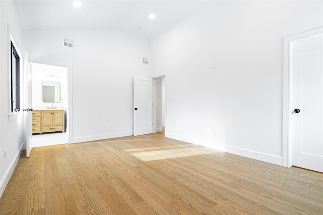 unfurnished bedroom featuring high vaulted ceiling, connected bathroom, and light hardwood / wood-style floors