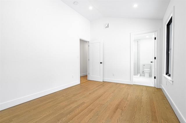 unfurnished bedroom featuring vaulted ceiling, connected bathroom, and light wood-type flooring